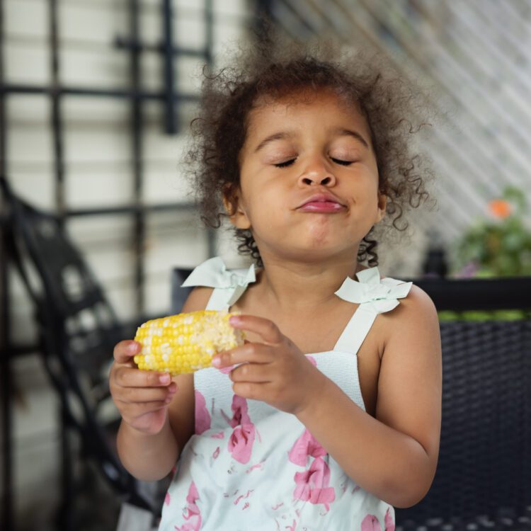 mixed-race-toddler-eating-corn-outdoors-in-summer-2